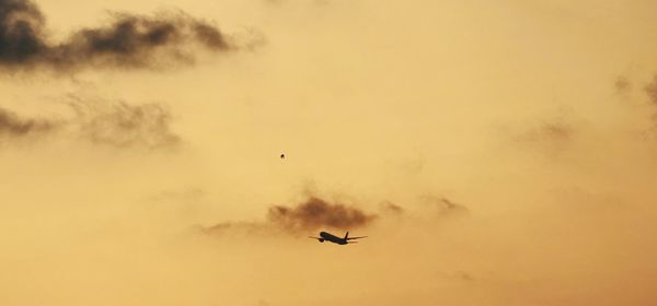 Low angle view of silhouette airplane flying against sky during sunset