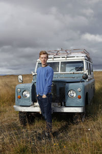 Portrait of confident man with hands in pockets standing against off-road vehicle against cloudy sky