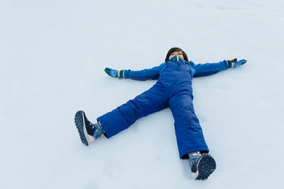 Child with dark hair in blue winter pants lying on the snow