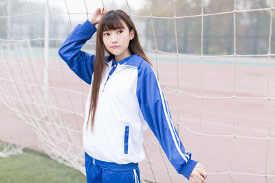 Young woman looking away while standing against net