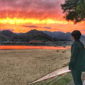 Man standing on field against orange sky