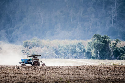 Tractor on plowed field against trees