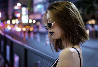 Young woman wearing sunglasses in city at night