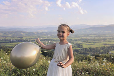 Portrait of smiling girl with balloon standing against landscape