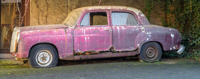 Abandoned vintage car parked by wall