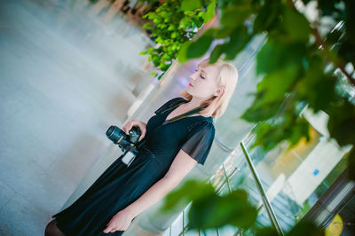 Portrait of young woman with camera in standing in building