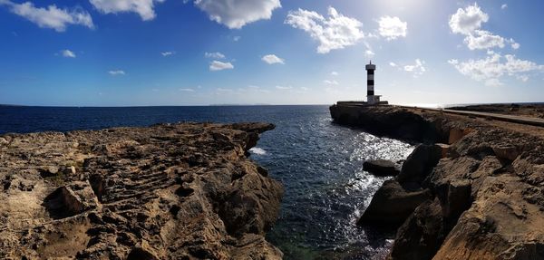 Lighthouse on rock by sea against sky