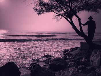 Silhouette man on rock at beach against sky during sunset