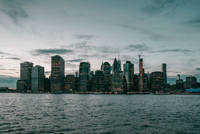 Illuminated city by sea against sky during sunset