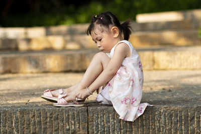 Girl wearing sandal while sitting on footpath