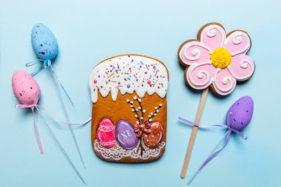 Gingerbread easter cake and flower, decorative easter eggs on sticks on light blue background. 