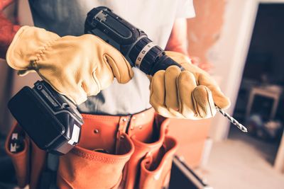 Midsection of carpenter wearing gloves holding drill