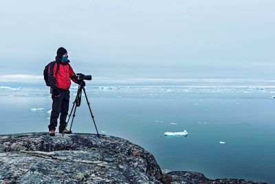 Scenic view of man on rock formation photographing frozen sea