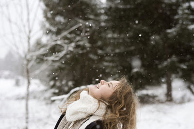 Happy young woman enjoying snowfall in winter forest