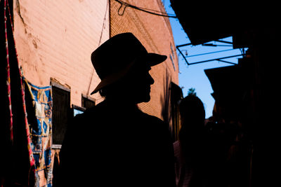 Side view of silhouette person standing against buildings and blue sky 