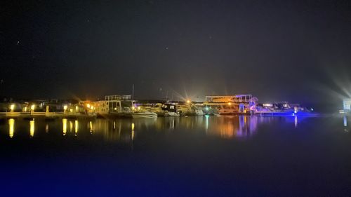 Illuminated city by sea against sky at night