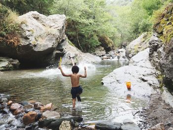 Rear view of shirtless boy running in river at forest