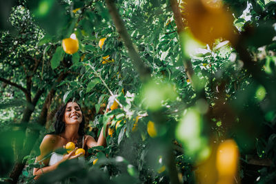 Young woman standing by tree against plants