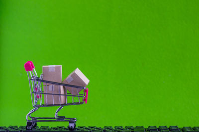Close-up of small shopping cart with packages on keyboard against green wall