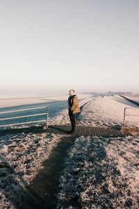 Side view of man standing on beach against clear sky during winter