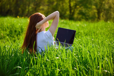 Woman using laptop while sitting on grassy field