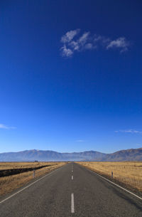 Road leading towards mountains against blue sky