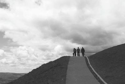 People walking on mountain against cloudy sky