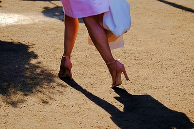 Low section of woman walking on dirt road during sunny day