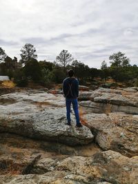 Rear view of man standing on rock against sky