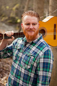 Man holding guitar standing by tree outdoors