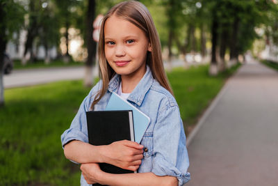 Smiling girl standing on street and holding notebooks. child outdoor. back to school concept.