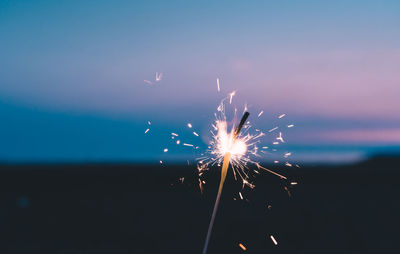 Lit sparkler against sky at dusk