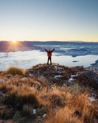 Rear view of man standing on shore against sky during sunset