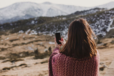 Rear view of woman using phone while standing on mountain