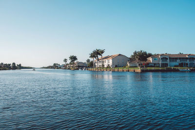 Buildings by river against clear blue sky