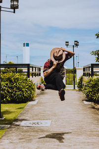 Man jumping on footpath against sky in city