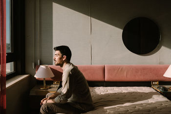 Side view of man sitting on bed at home