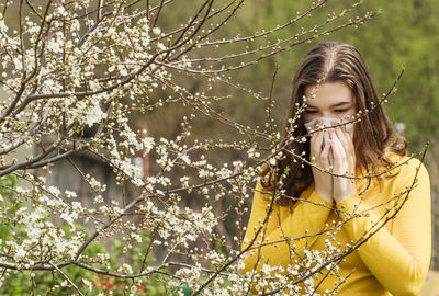 Portrait of woman with pink flowers against tree