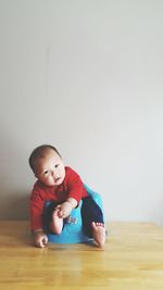 Cute baby boy sitting on seat against wall at home