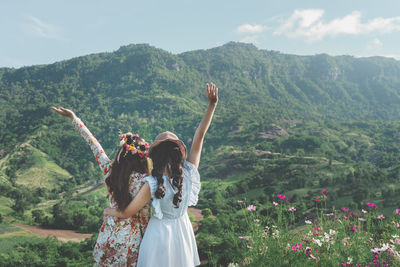 Rear view of women standing by flowering plant against mountain