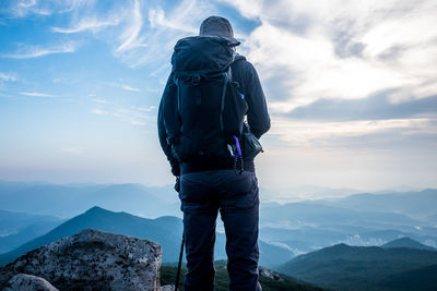 Rear view of male hiker standing on mountain against sky