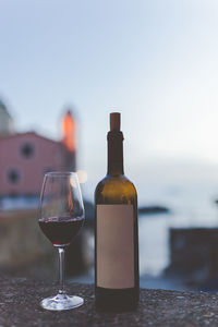 Close-up of wineglass and bottle on retaining wall against sky