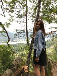 Portrait of woman standing by tree in forest