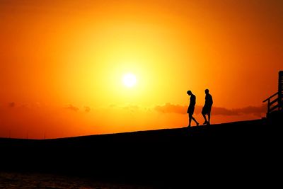 Silhouette men standing on land against sky during sunset