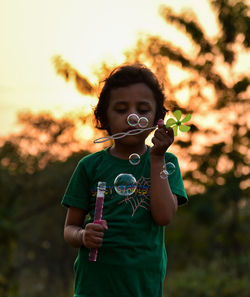 Girl blowing bubbles while playing in park during sunset