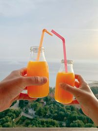 Close-up of hand holding drink at sea against sky