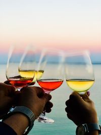 Close-up of hand holding wine glasses against sky during sunset