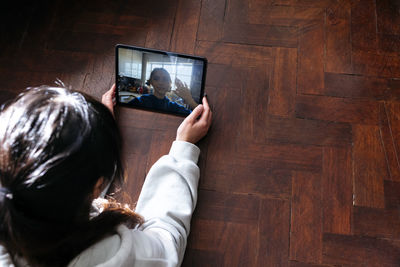 Young woman talking with friend waving over video call using tablet pc on hardwood floor
