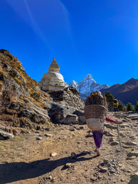 Nepalese porter with load of firewood walking on path with monument