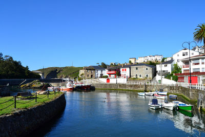 Boats moored in canal by buildings against clear sky